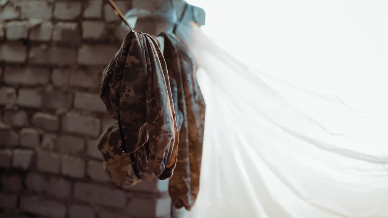 Close up of camouflage cloth hanging on wire indoors near brick wall with sunlight filtering through curtain, fabric folds creating texture and atmosphere reflecting daily life