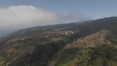 vista aérea de la parroquia de calheta en la isla de madeira portugal, drone girando a la derecha mostrando la casa en la cima de la montaña y algo de niebla pasando a través de la cámara
