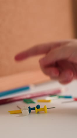 child hand touches bright colorful pins near pencils. junior schoolgirl chooses pin with red flag preparing to attach note to cork board. pupil plans studies