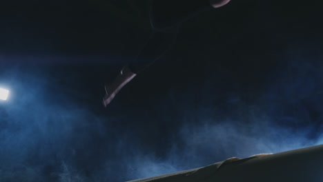 close-up of the foot of a girl professional gymnast performs a jump with rotation on the balance beam in slow motion. smoke blue color in the gym. gymnastics competitions