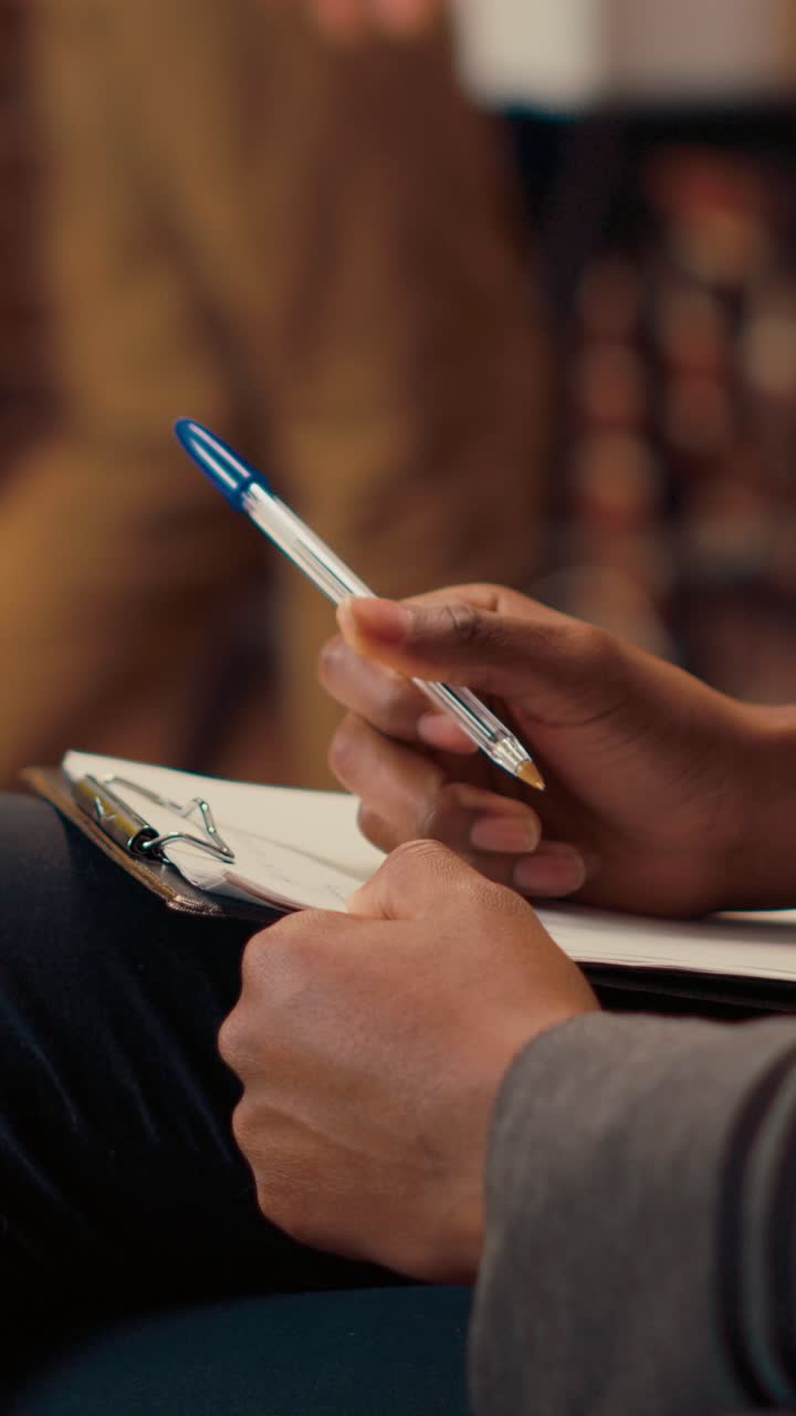 Vertical video: Psychotherapist taking notes on papers and listening to man