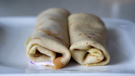 caucasian man placing rolled crepes filled with blueberry cream on a white plate