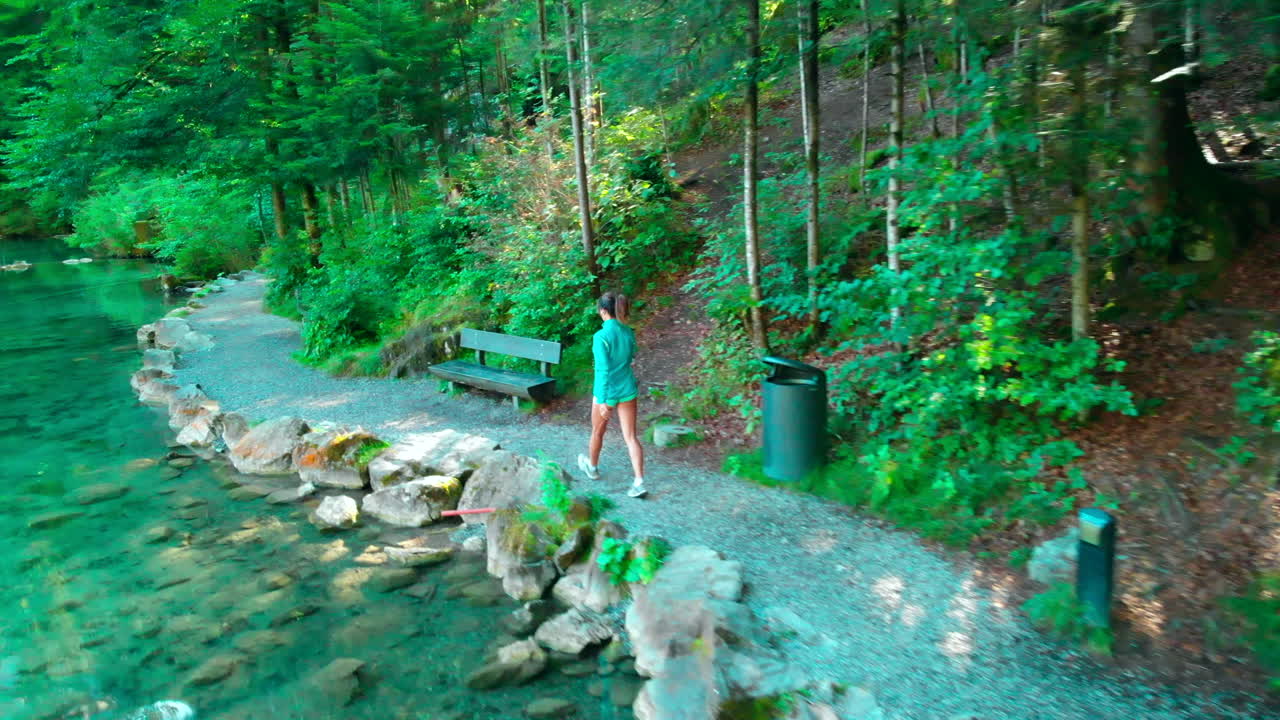 disparo de drones siguiendo a una mujer deportiva mayor caminando por un hermoso lago en la naturaleza