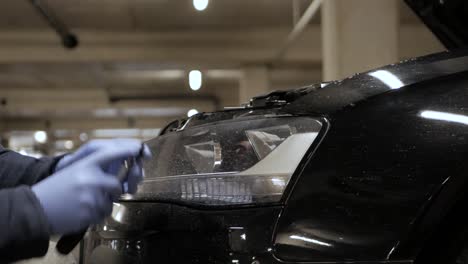 Unscrewing-headlamp-wearing-hand-gloves-in-a-parking-lot,-closeup