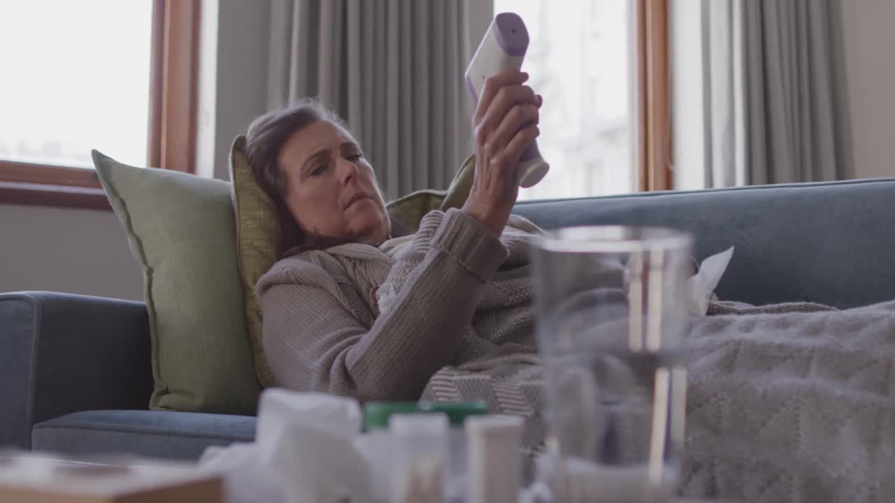 Kvinne måler temperaturen sin mens hun ligger på sofaen hjemme