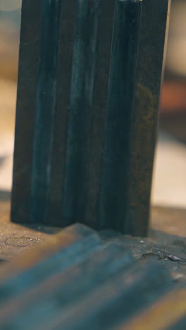 cu: jeweler takes gold bar with tweezers from form on table with asbestos sheet in manufacturing workshop close view
