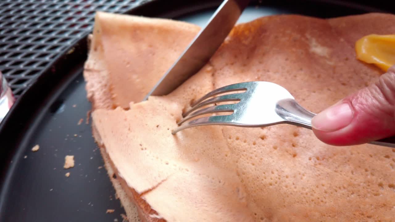 Handheld shot of hands cutting a pancake with a fork and a knife, outdoor, close up shot