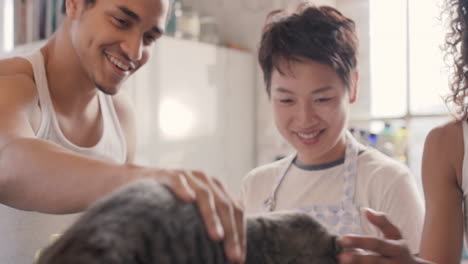 diverse group of student friends playing with cat making breakfast pancakes wearing pyjamas at home in kitchen