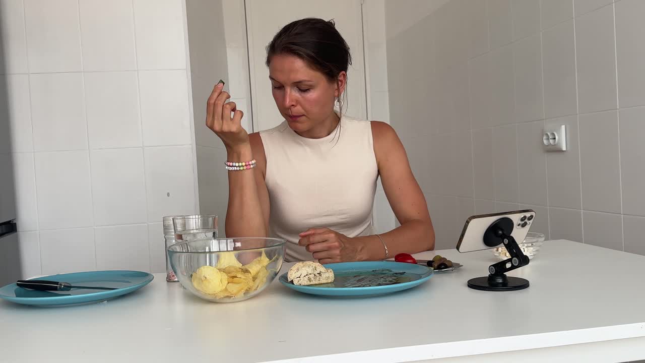 Giovane donna che mangia olive e patatine mentre guarda il telefono