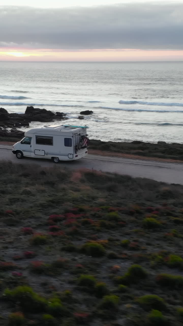 Furgoneta camper conduciendo por una pintoresca carretera costera al atardecer.