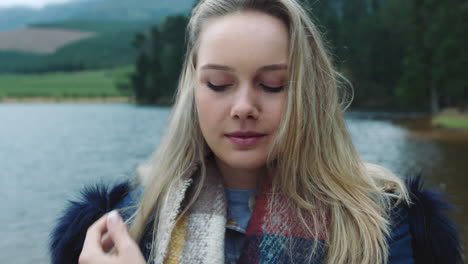 retrato de una hermosa mujer rubia con expresión seria en un frío día de invierno al aire libre junto al lago con el viento soplando el pelo 4k