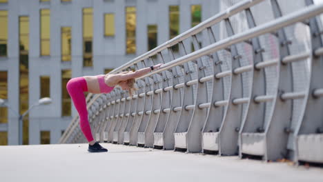 Joven-Mujer-Rubia-En-Ropa-Deportiva-Rosa-Se-Estira-En-El-Puente,-Amplia