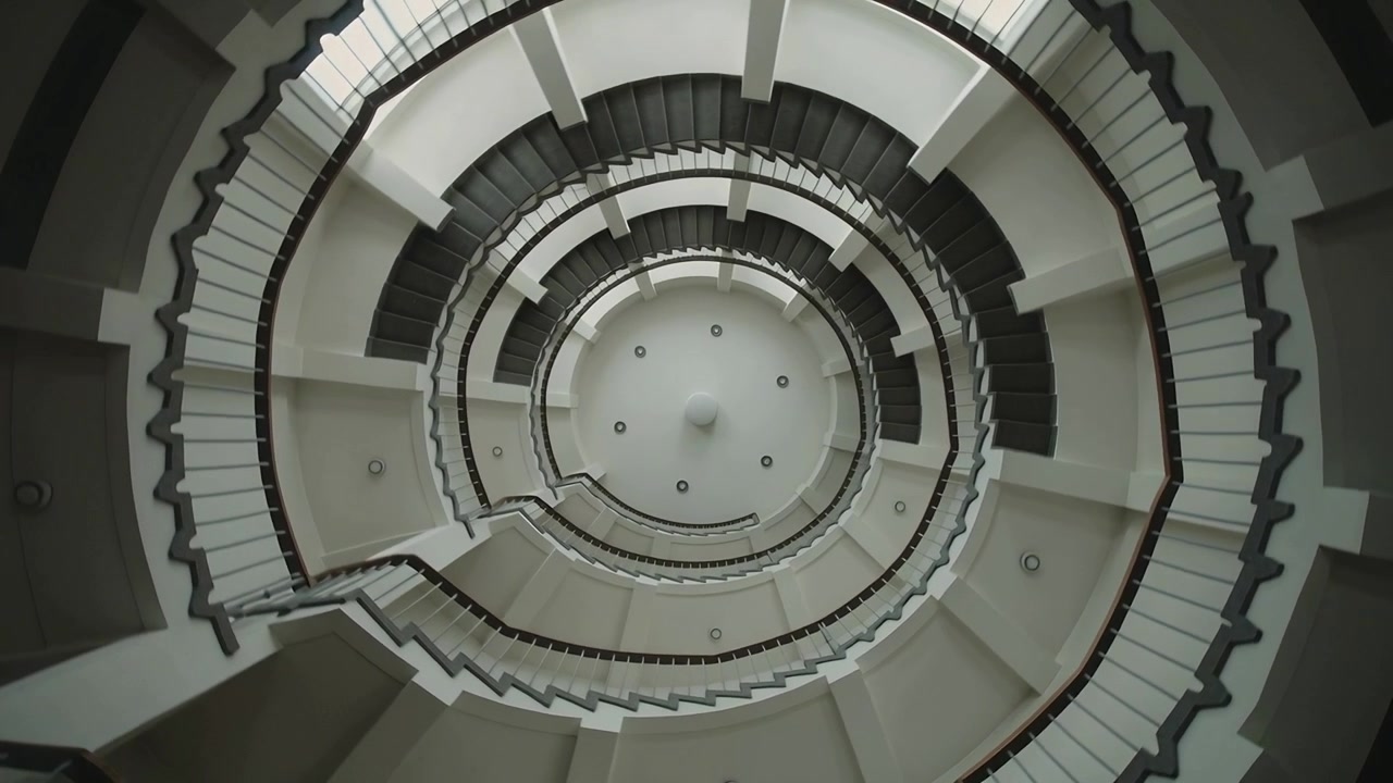 Rotating camera capturing multi-level spiral staircase in atrium, revealing handrails, ceiling disk