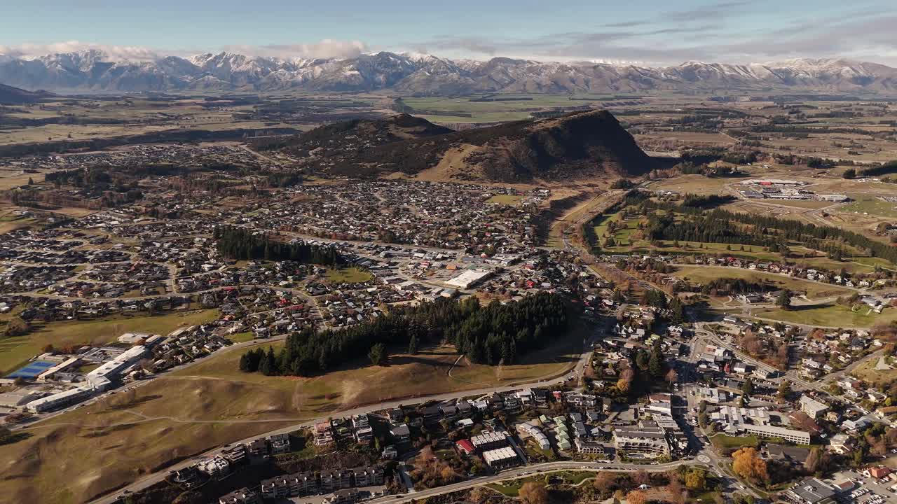 High aerial establishing shot of Wanaka town nestled in valley with snow-capped Southern Alps mountain range in background, New Zealand