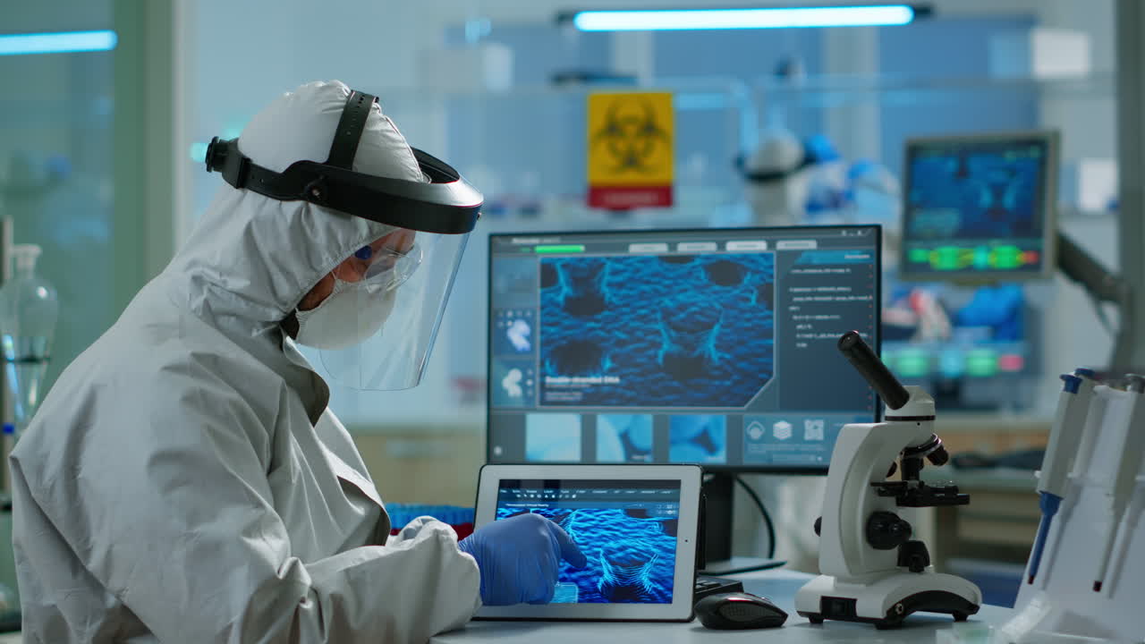 태블릿을 사용하여 백신을 개발하기 위해 일하는 커버올을 입은 화학자