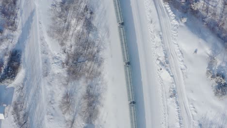 a birds eye view of a snowy train travelling through the forests in the canadian shield