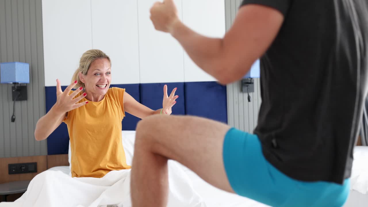 Donna gioiosa guarda uomo in pantaloncini che balla in camera da letto, filmato 4k