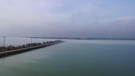 Aerial-dolly-along-highway-bridge-crossing-large-body-of-water,-cityscape-covered-in-fog-in-the-distance