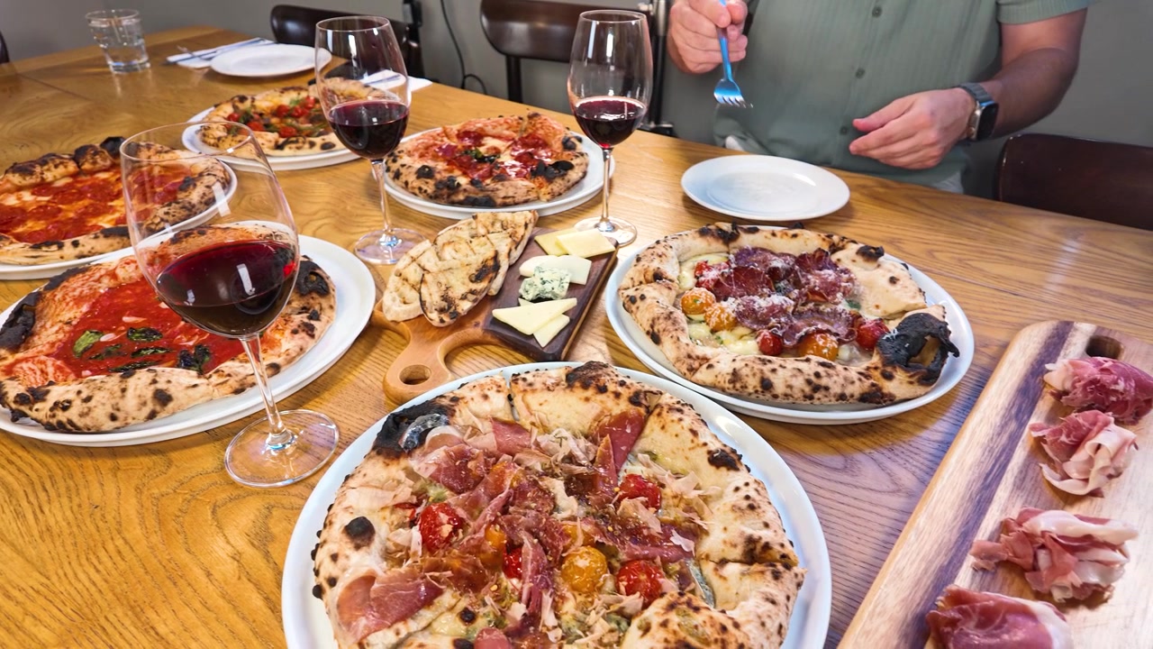 Draufsicht auf Menschen, die im Restaurant handgemachte Pizzen, Rotwein und Käse genießen.