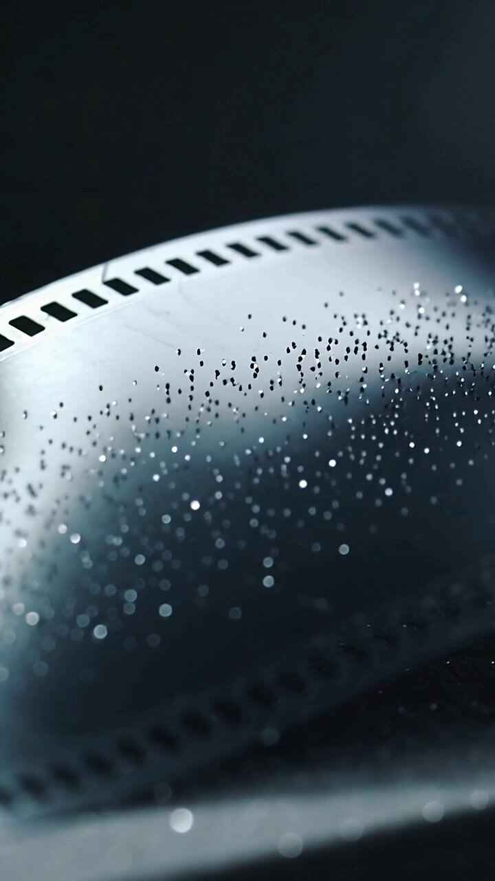 Vertical video: Moving curved film strip after camera move in studio showing droplets and sprockets