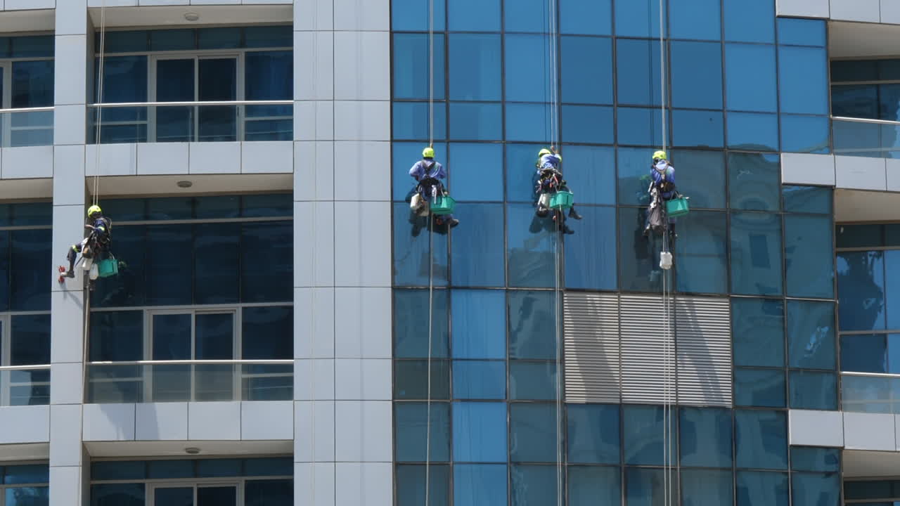 los limpiadores de ventanas lavan el vidrio en la pared de un edificio de oficinas en un rascacielos - tiro de ángulo bajo