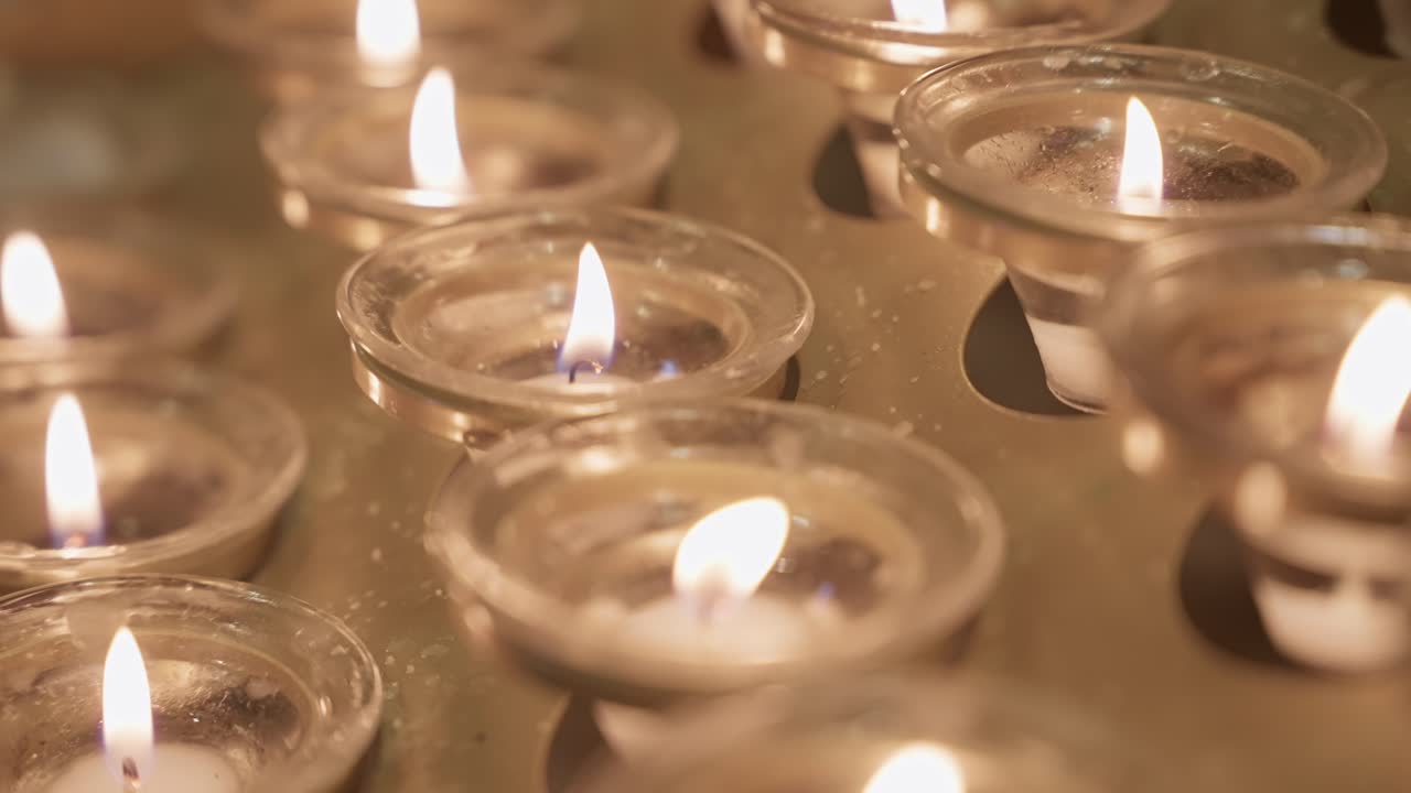 Velas de oración que brillan suavemente en primer plano, simbolizando la fe y el recuerdo