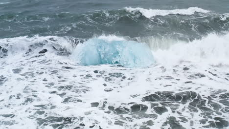 Atemberaubende-Drohnenaufnahme-Von-Wellen,-Die-Auf-Einem-Wunderschönen-Eisfelsen-Am-Diamond-Beach-In-Island-Brechen