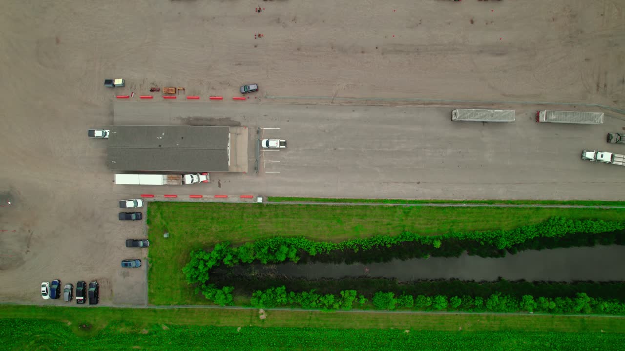 Top-down aerial view of flatbed semi-trucks at the check-in guard station of an industrial plant.