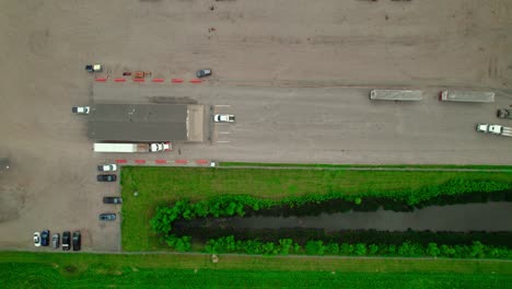 top-down aerial view of flatbed semi-trucks at the check-in guard station of an industrial plant.