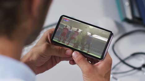 compuesto de un médico masculino viendo un partido de hockey en un teléfono inteligente