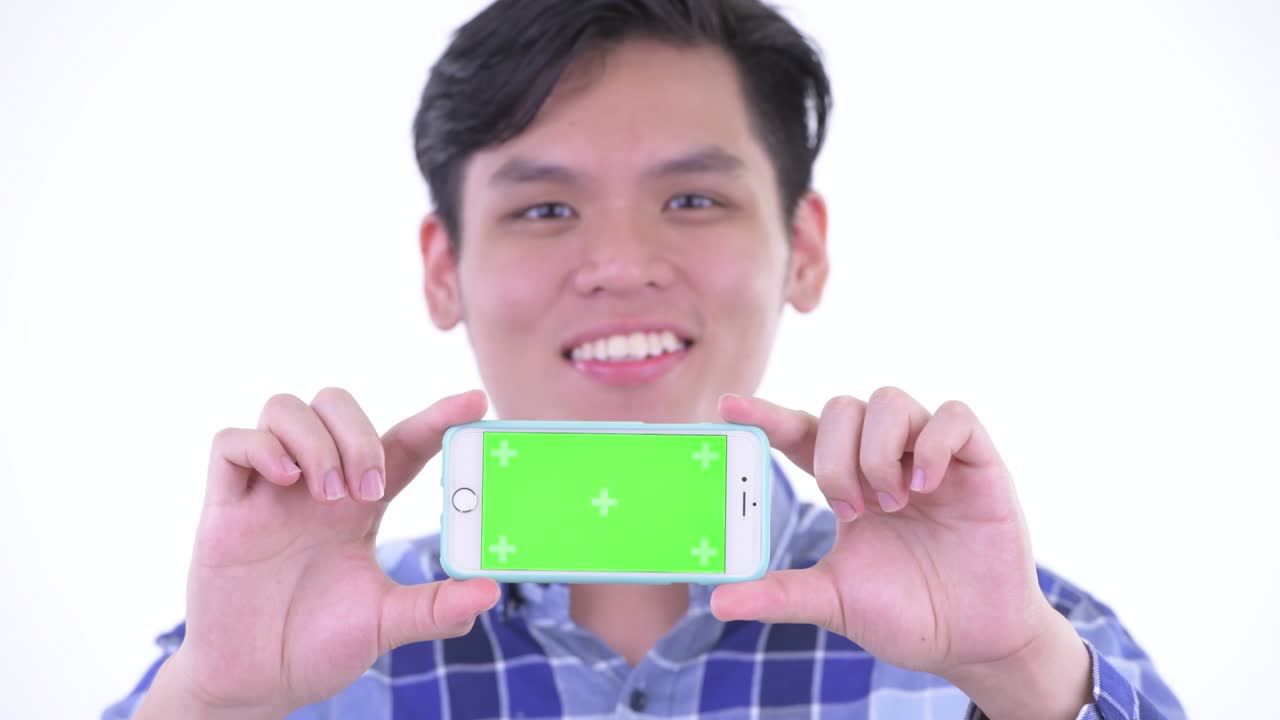 젊은 잘생긴 아시아 남자의 초상화  바탕에 고립 된 복사 공간과 함께 휴대 전화를 보여줍니다.