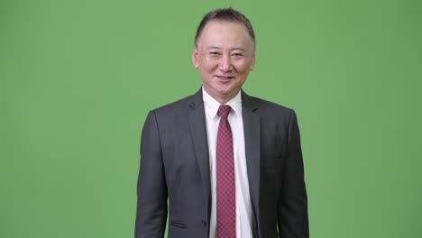 mature japanese businessman giving handshake against green background