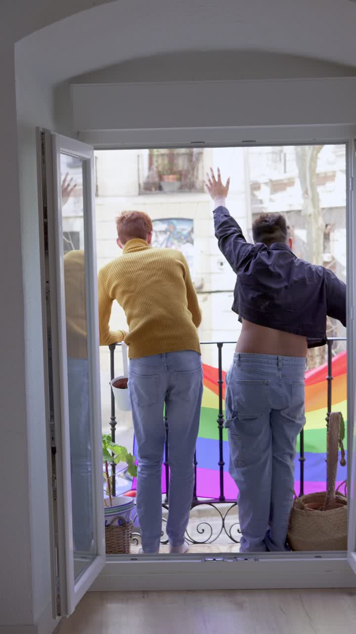 Two people on a balcony with a vibrant rainbow pride flag