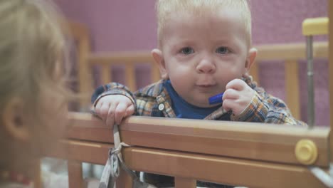 little girl gives marker cap to junior brother in wooden cot