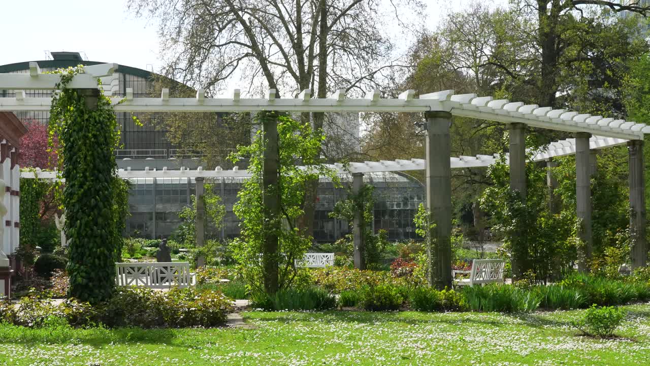Palmengarten Frankfurt med pergola, statuer og drivhus omgivet af frodigt grønt og blomstrende planter i forårsdagslys