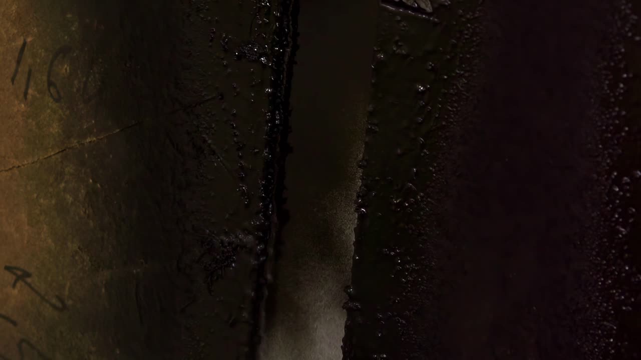 Close up handheld footage of a dark coated metal component with textured industrial surface and narrow light gap