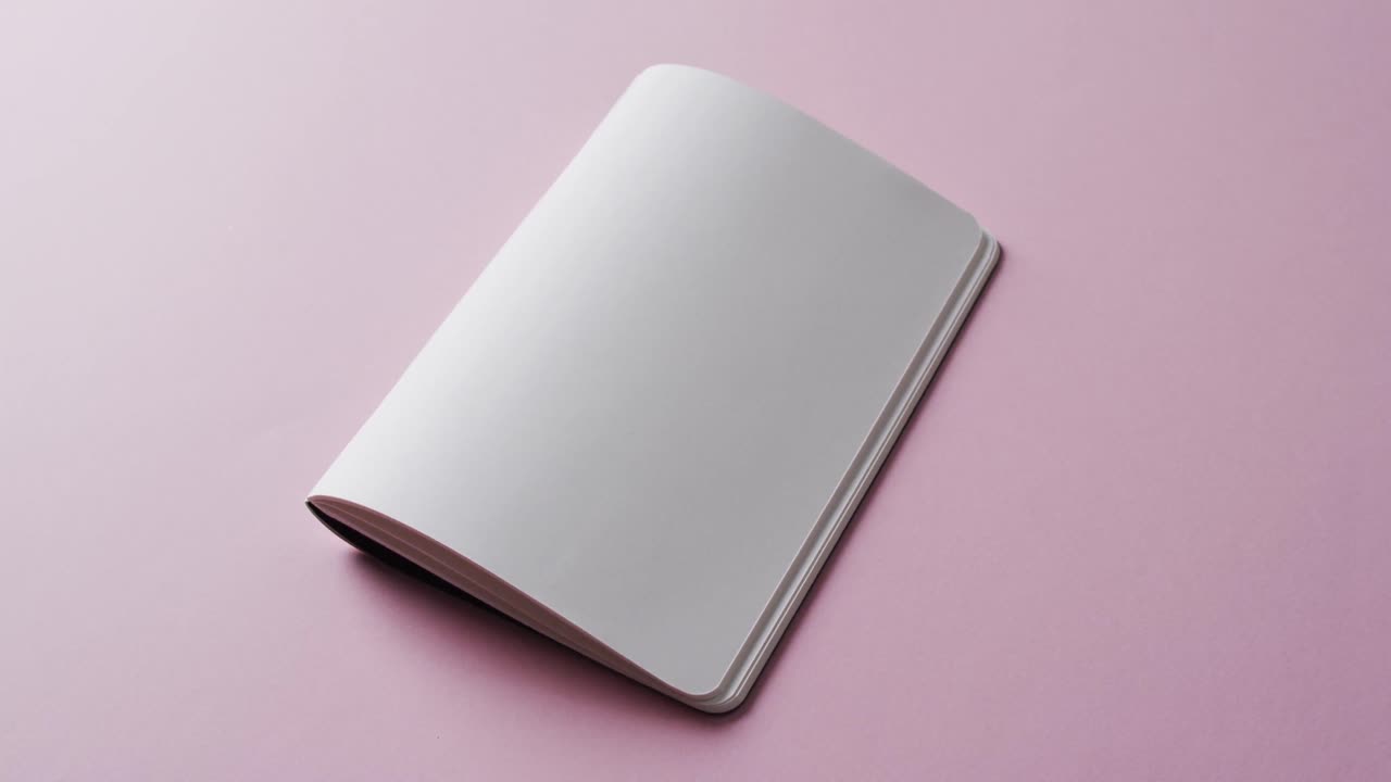 Close up of open blank book with copy space on pink background in slow motion