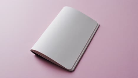 Close-up-of-open-blank-book-with-copy-space-on-pink-background-in-slow-motion