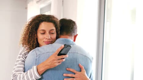 Linda-Pareja-Usando-Un-Teléfono-Inteligente-Mientras-Se-Abraza-En-La-Sala-De-Estar