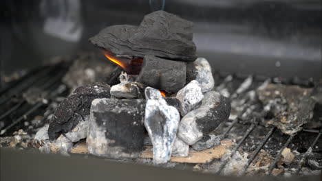 Zeitlupen-Nahaufnahme-Eines-Haufens-Holzkohle,-Der-Mit-Einer-Kleinen-Flamme-Und-Etwas-Rauch-Zu-Brennen-Beginnt