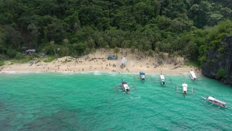 Drone-flying-towards-beautiful-white-sand-secret-beach-with-huge-limestone-cliffs,-turquoise-water,-small-boats-and-natural-archipelago-paradise-in-El-Nido,-Palawan,-Philippines