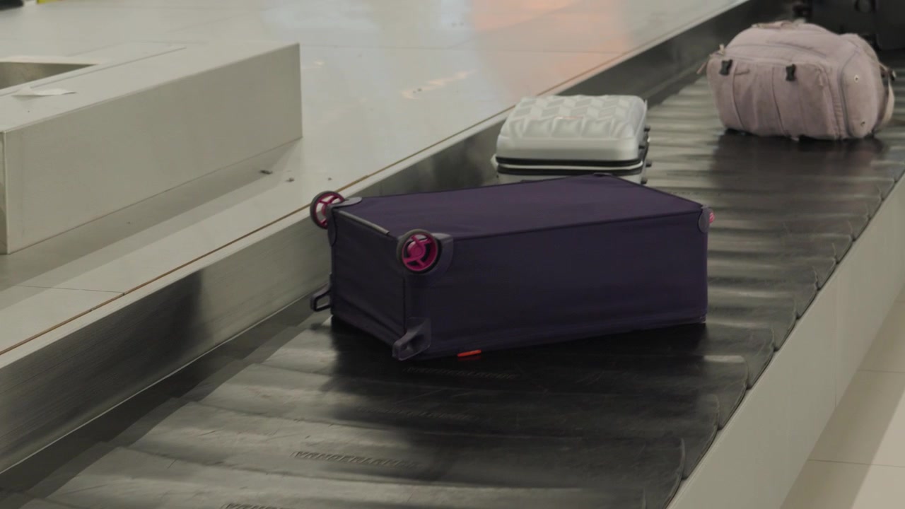 Si vedono le valigie arrivare sul nastro trasportatore dei bagagli. I viaggiatori attendono nelle vicinanze per ritirare i loro bagagli dopo l'arrivo in aeroporto. L'ambiente mostra l'atmosfera frenetica dell'area di ritiro bagagli.