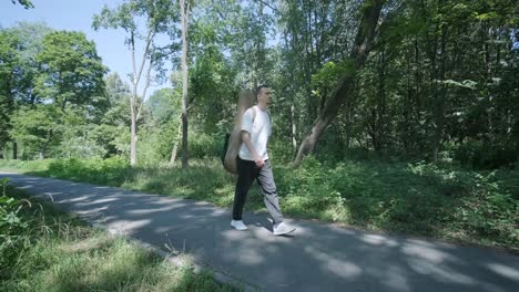 young man walking with guitar on street near forest