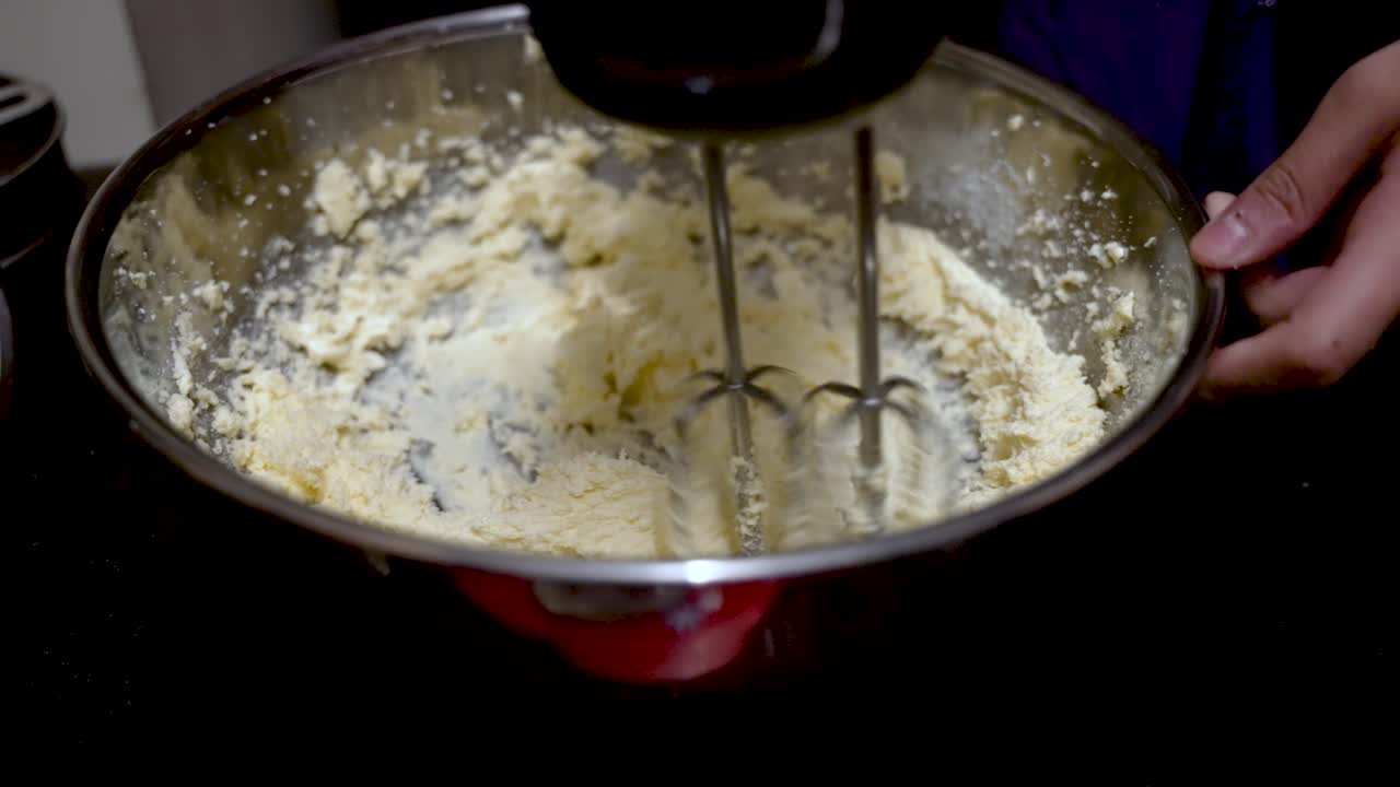Whisking dough mixture in a stainless steel bowl using an electric hand mixer.