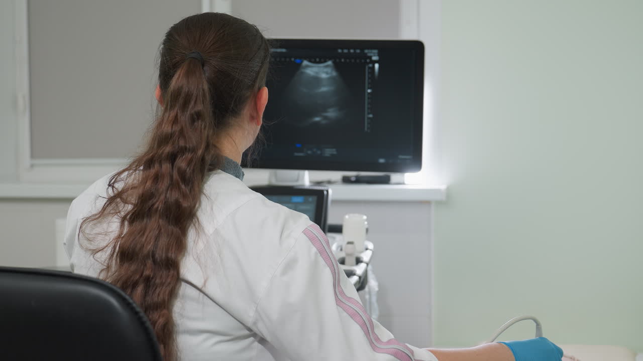 Female lab technologist focuses intently on monitor displaying patient internal organ movement during diagnostic procedure using advanced medical equipment in bright clinical setting with precision