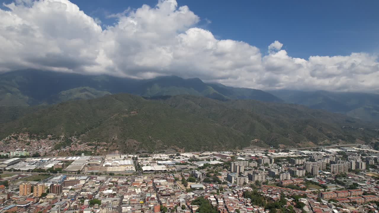 Guarenas cityscape with lush mountains under a bright, cloudy sky, aerial view