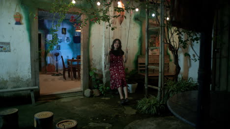 a happy young asian woman swings outside her home at night, wide shot