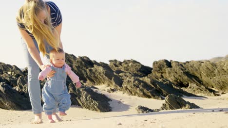 front view of mid adult caucasian mother helping baby to walk at beach on a sunny day 4k