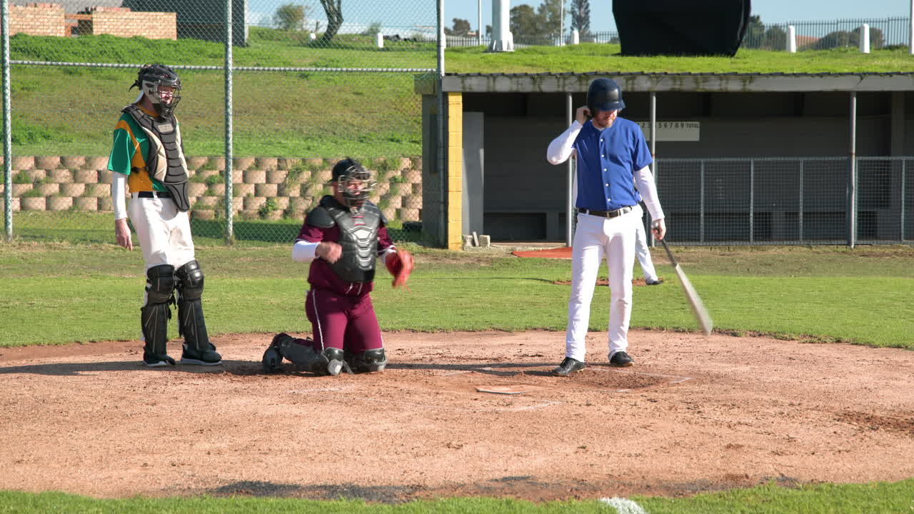 Durante una partita di baseball, il battitore si sistema il casco mentre il ricevitore e l'arbitro osservano attentamente.