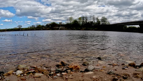 water from river touches gently against river rocks in sand on cloudy day, timelapse